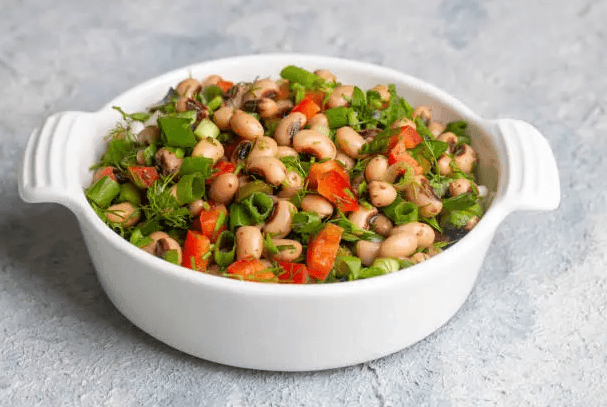 Colorful dense bean salad with chickpeas, black beans, kidney beans, and fresh vegetables like tomatoes and parsley in a glass bowl, served on a wooden table.