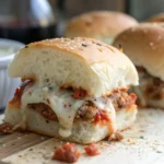 Golden-brown meatball sliders topped with melted mozzarella and fresh parsley on a serving tray.