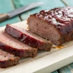 Smoked meatloaf with a rich BBQ glaze on a wooden cutting board, garnished with fresh parsley and surrounded by smoked vegetables.